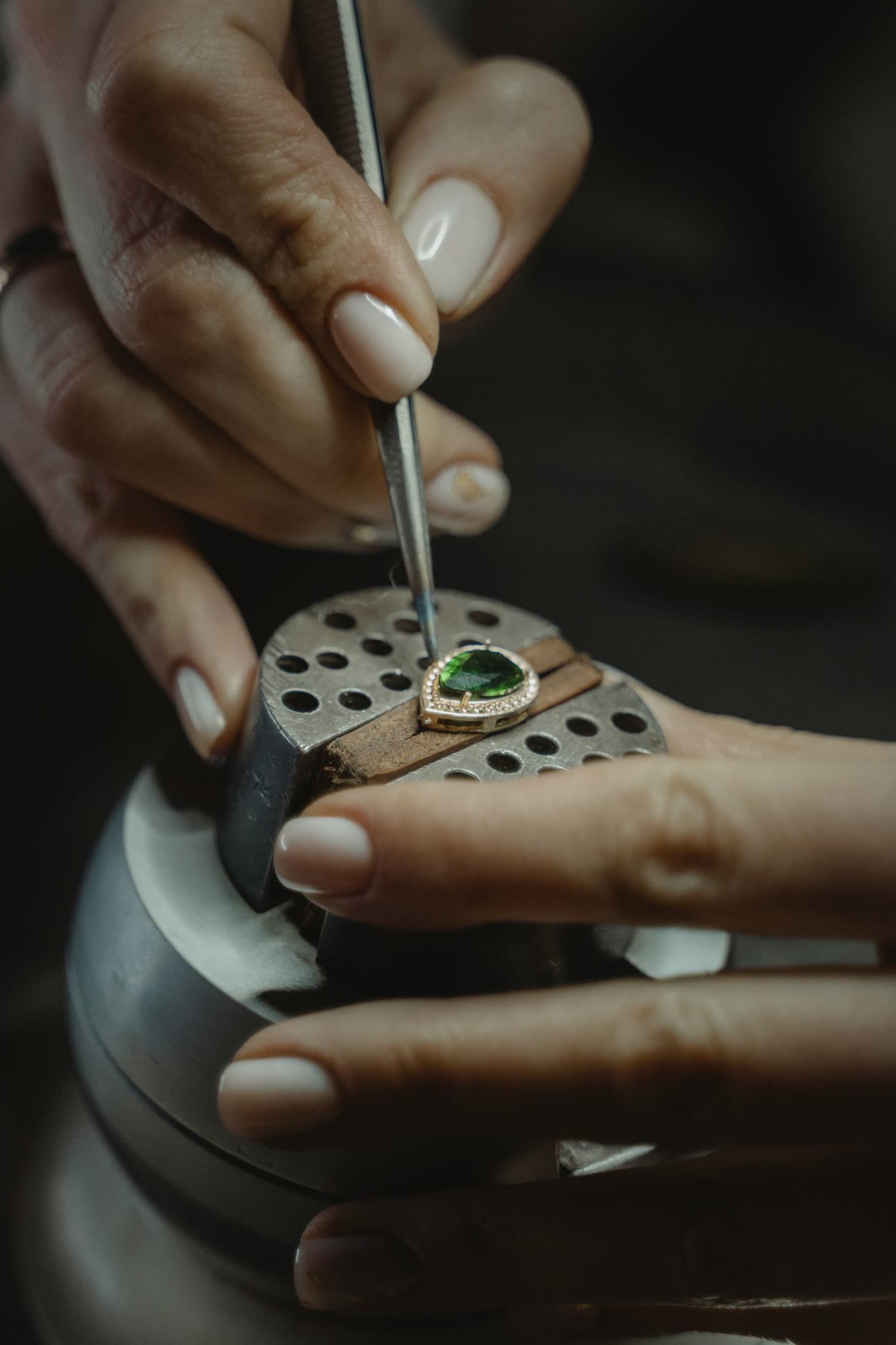 A jeweler using tweezers to set a green gemstone into a ring at a workbench