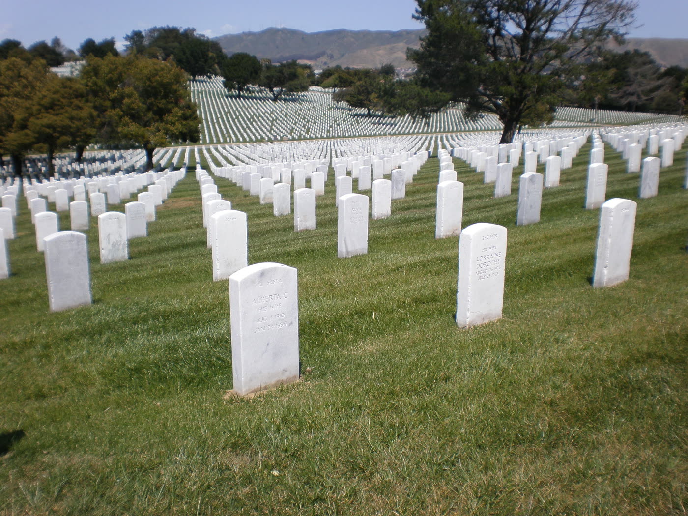 Rows of small upright white marble markers on a grassy hillside at Golden Gate National Cemetery