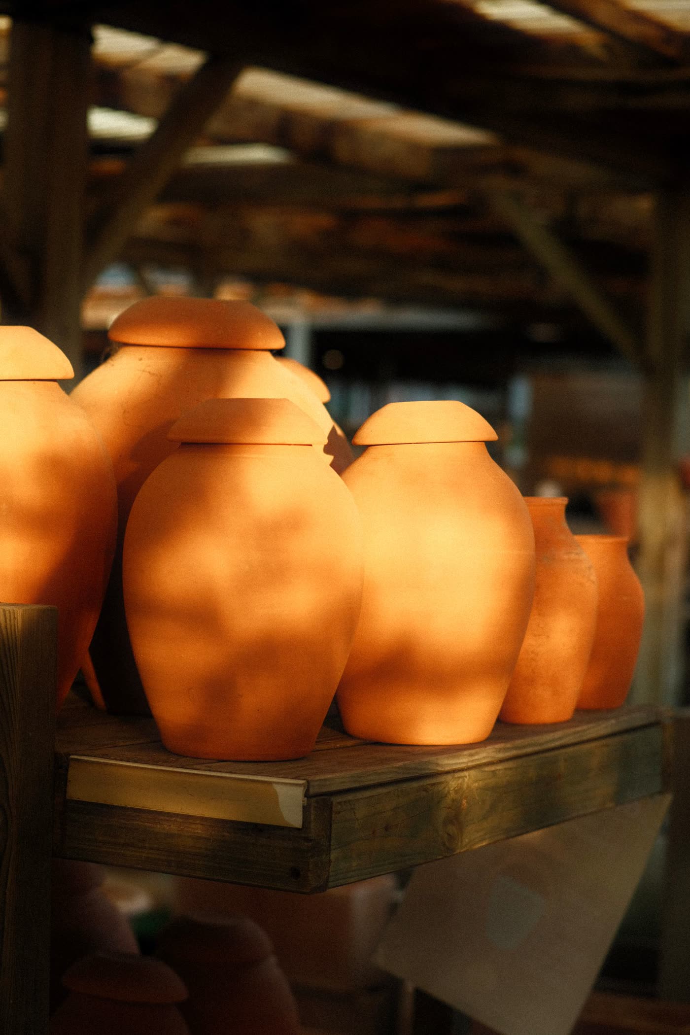 Rows of unglazed terracotta urn-shaped vessels with fitted lids on a wooden shelf
